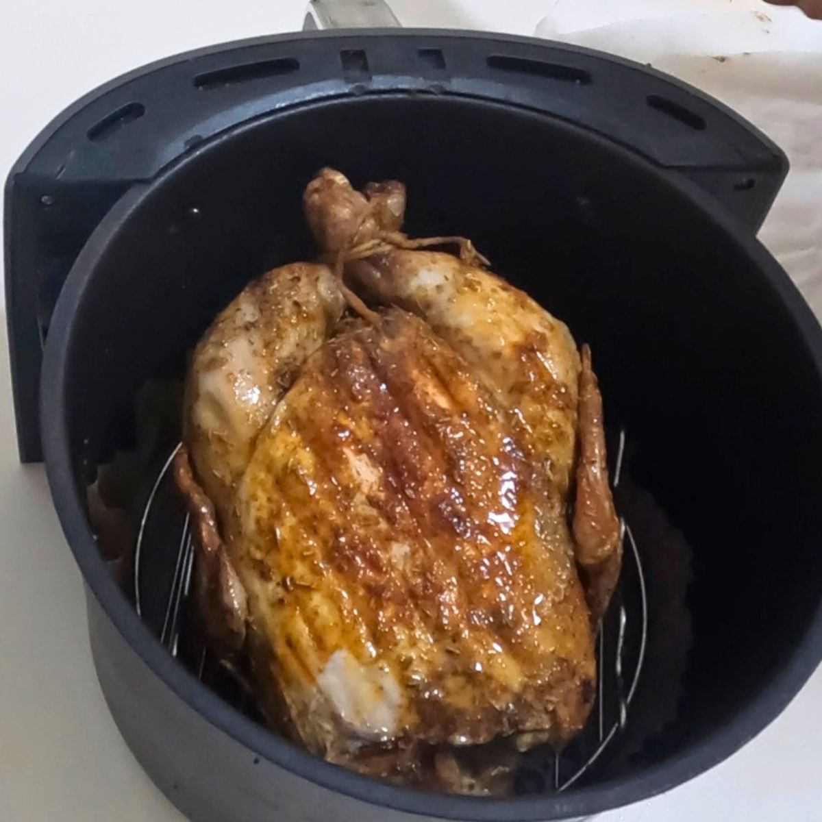 Air fryer basket with roasted whole chicken.