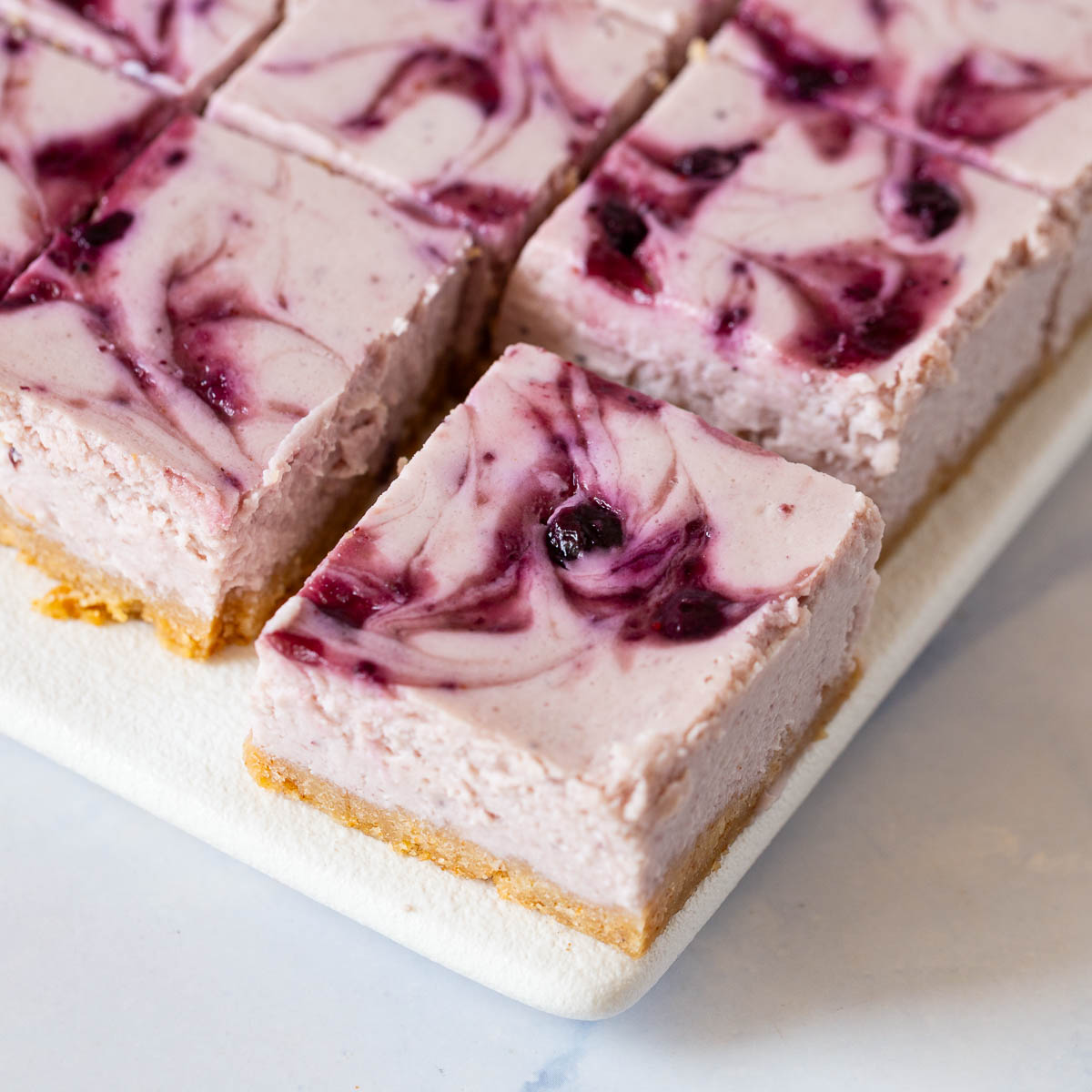 Cheesecake bars with blueberry swirl on the tray.