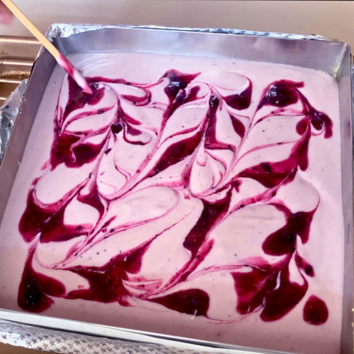 Cheesecake batter with blueberry swirl in pan.