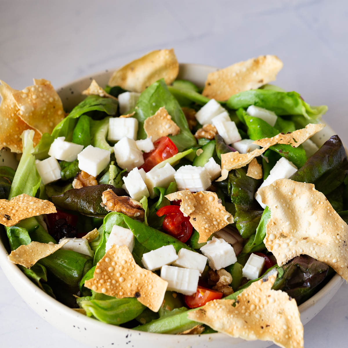 A bowl with salad made with butter lettuce and feta and chicken.