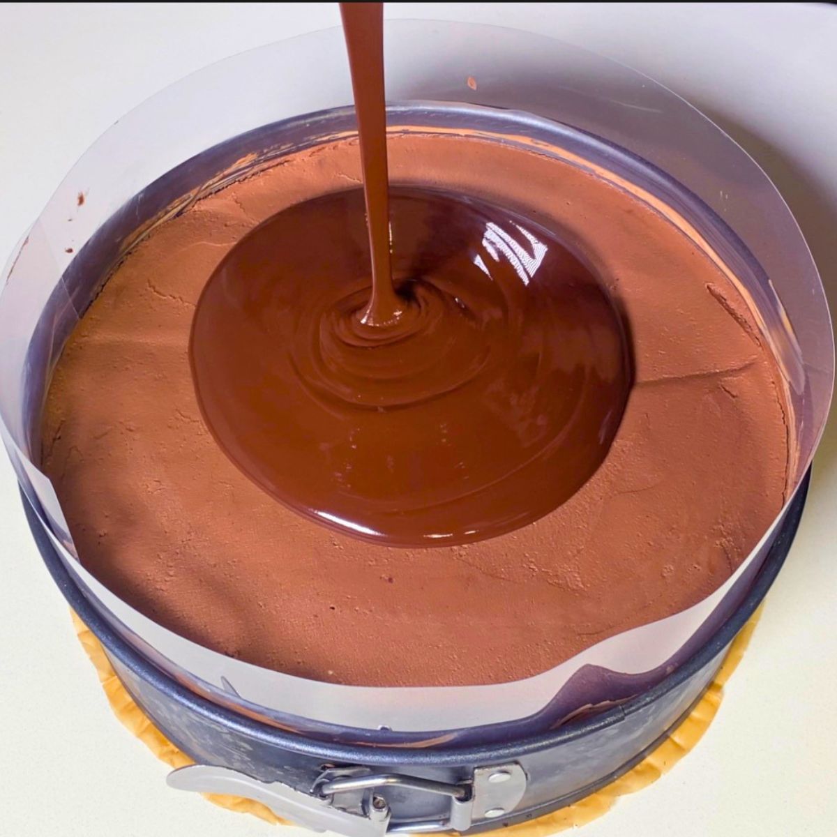 Pouring chocolate glaze over the mousse cake.