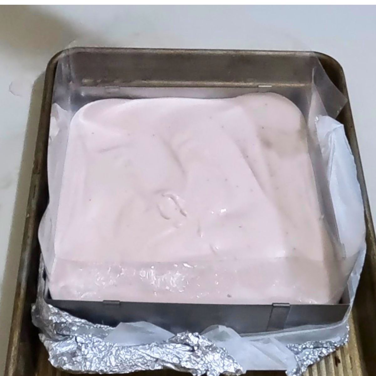 A square baking pan with pink strawberry mousse.