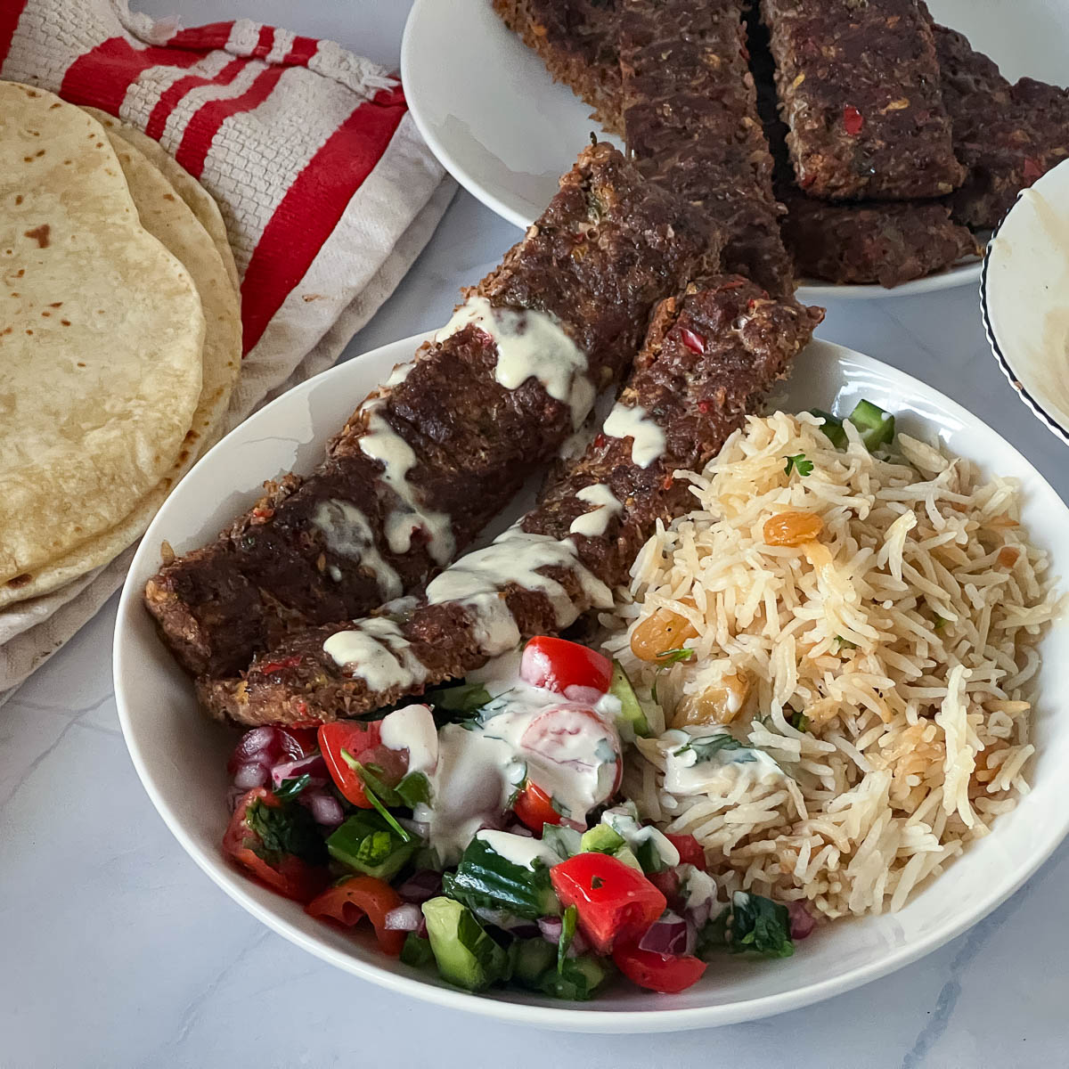 A plat with rice salad tahini and ground beef kebabs.