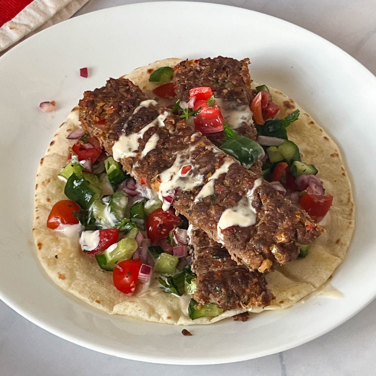 Ground meat kebabs over flatbread salad and tahini.