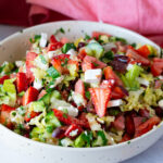 A bowl with salad and chopped strawberries.