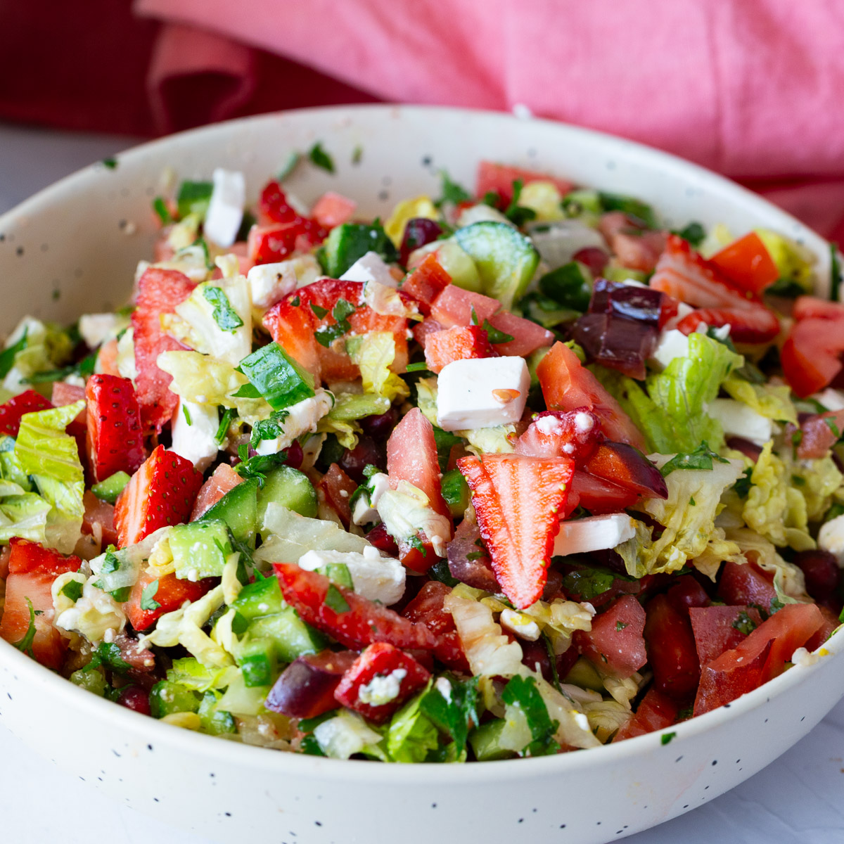 A bowl with salad and chopped strawberries.