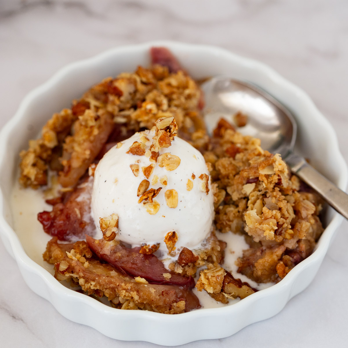 A white ramekin with fresh peach crisp with ice cream.