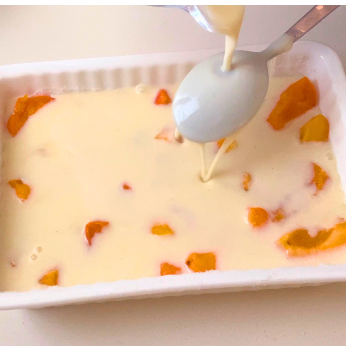 Pouring custard batter over apricots for clafoutis.