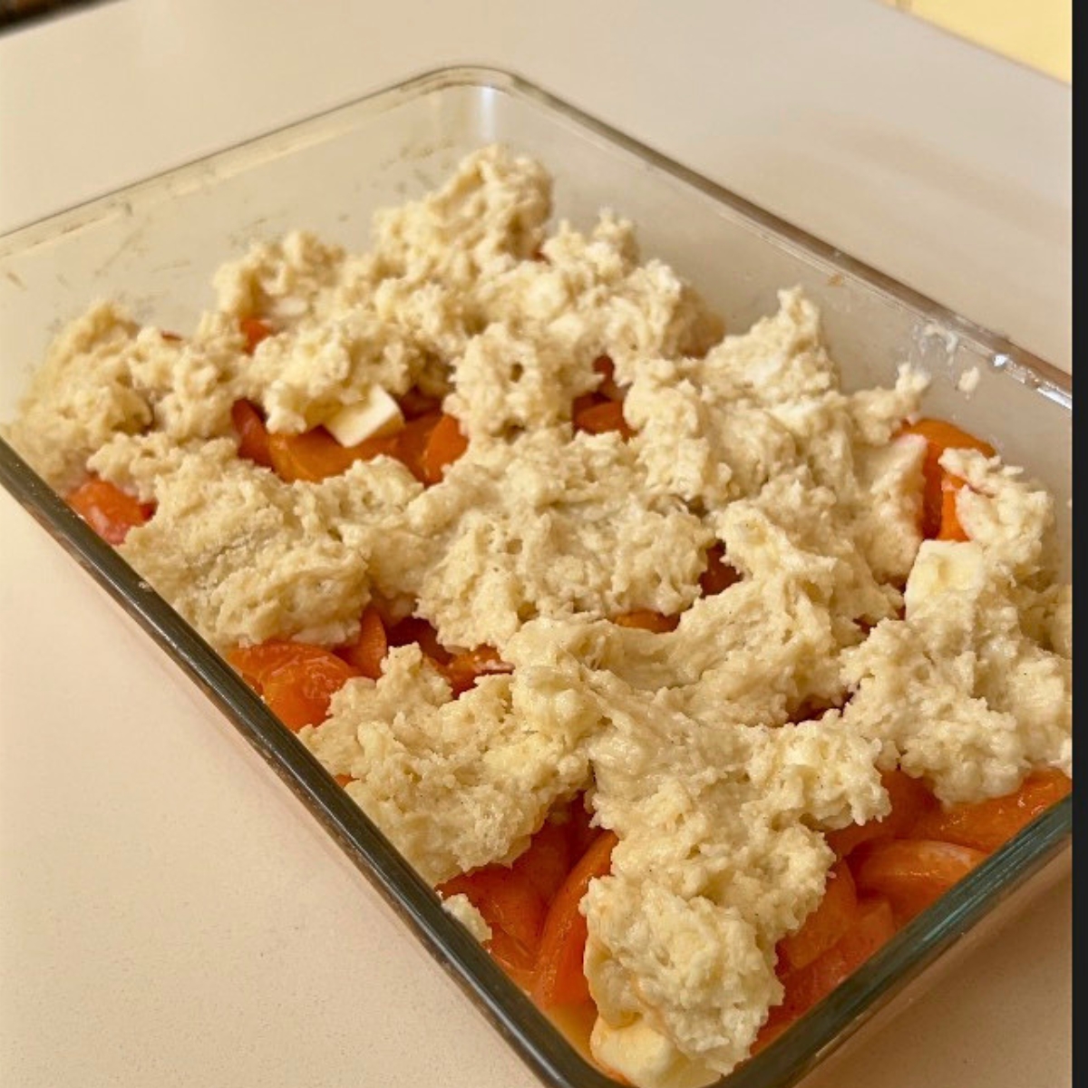 A baking dish with fresh apricots and cobbler topping.