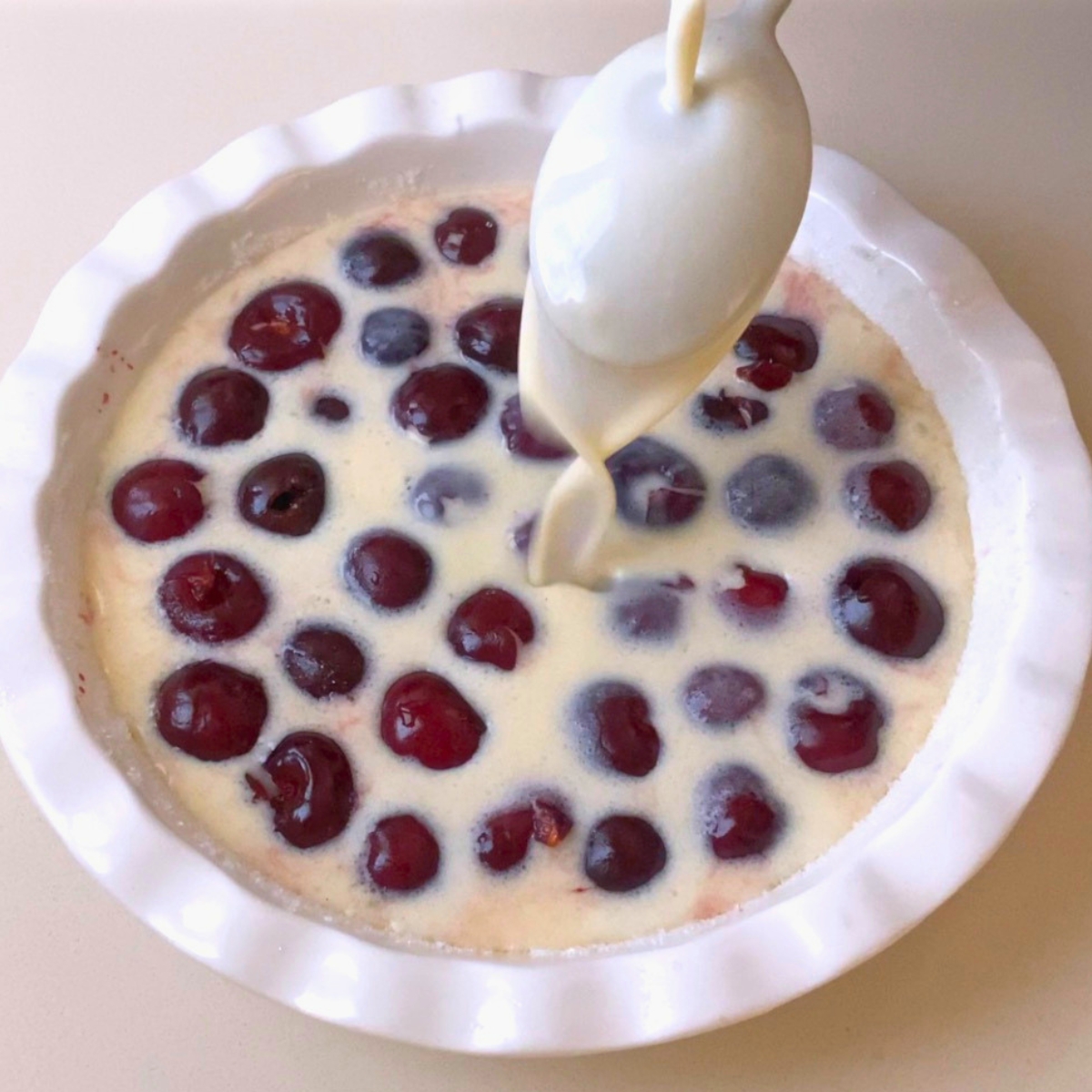 Pouring custard over fresh pitted cherries.