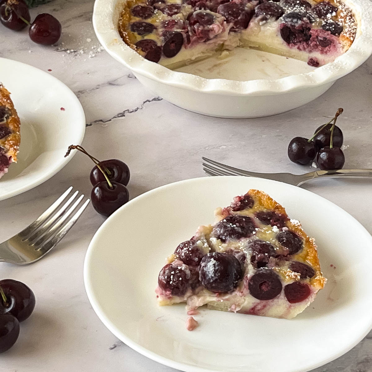Cherry clafoutis slices on white plates.