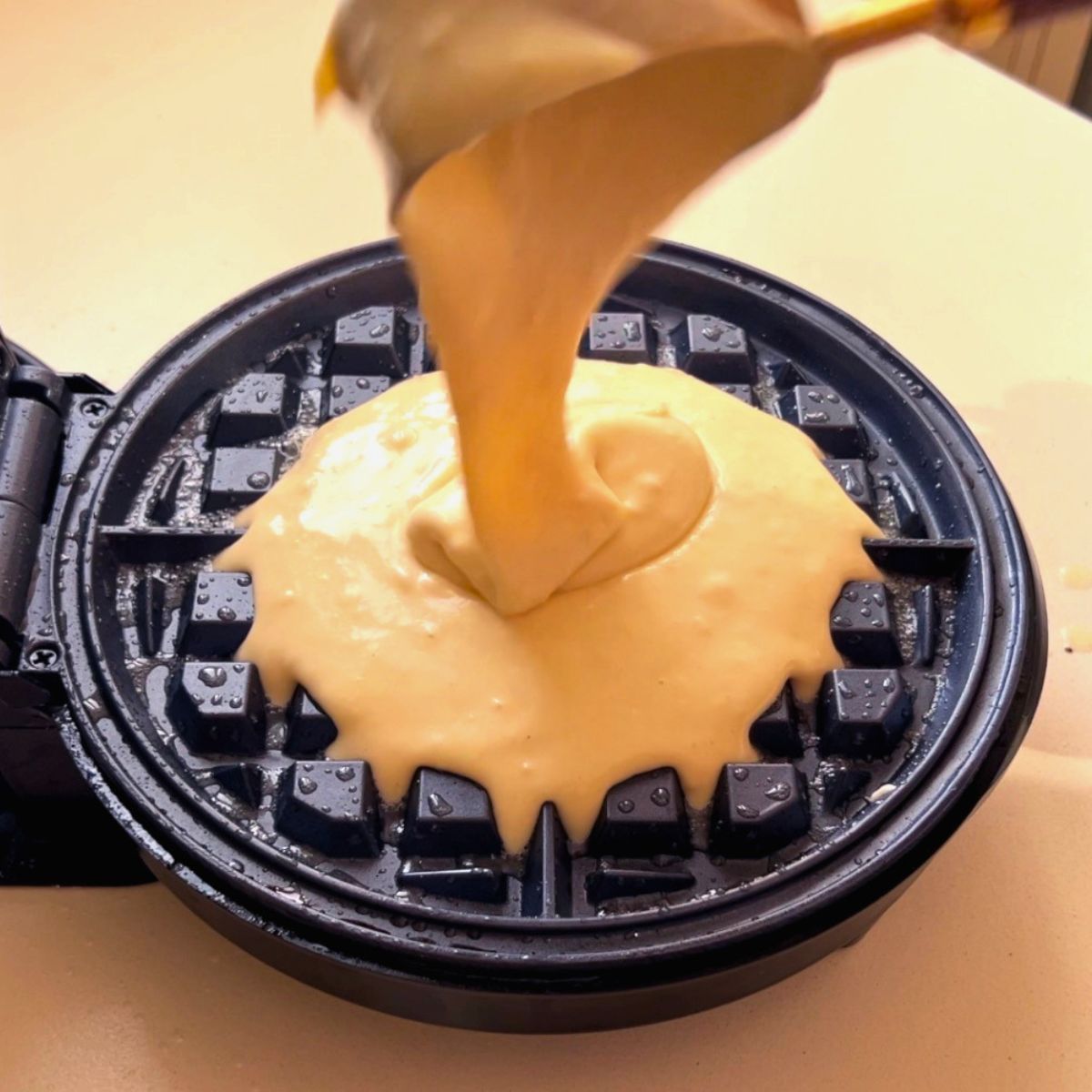Pouring waffles over a waffle iron.