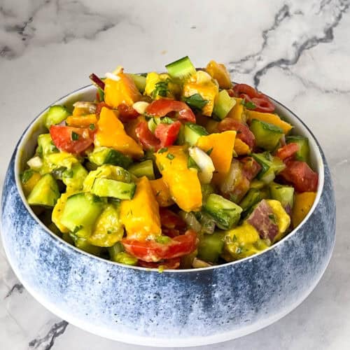 A blue bowl with mango salad and lime dressing.