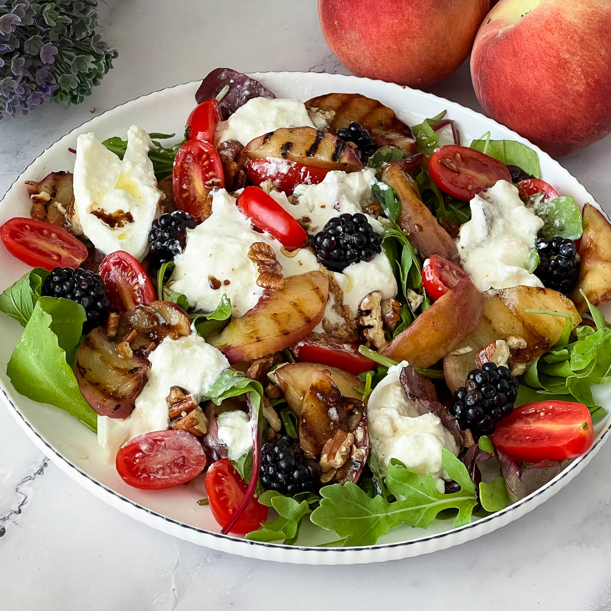 A white plate with fresh peach salad with burrata.