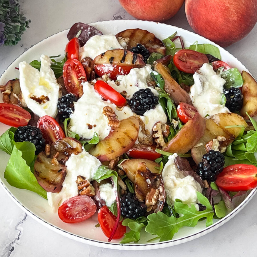 A white plate with fresh burrata salad and grilled peaches.