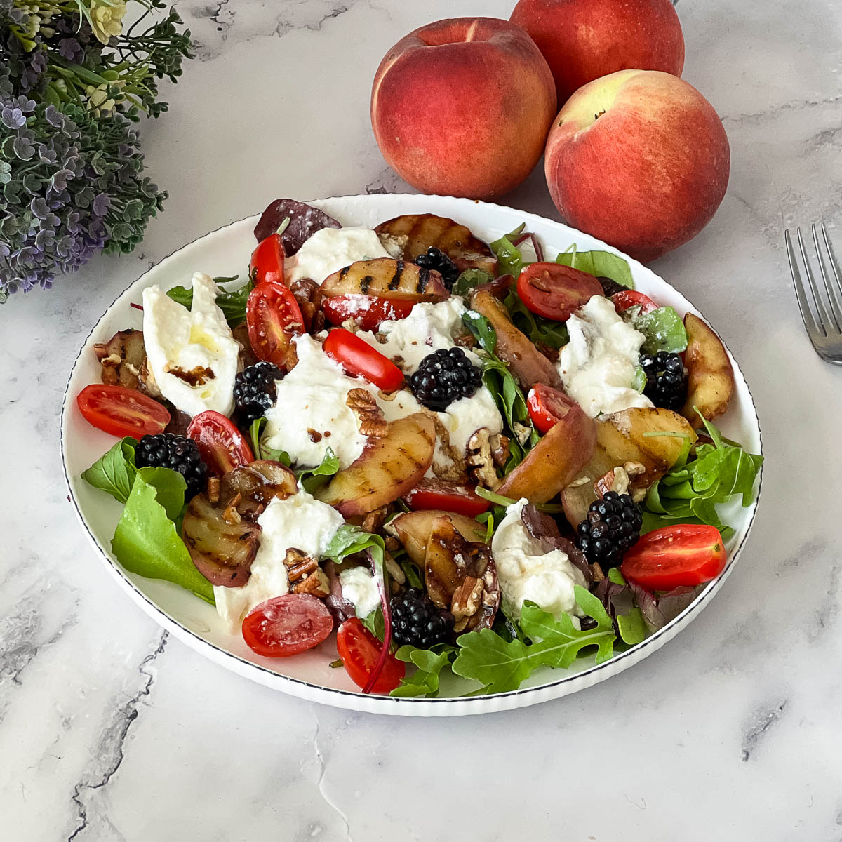 A white plate with burrata over peach salad.
