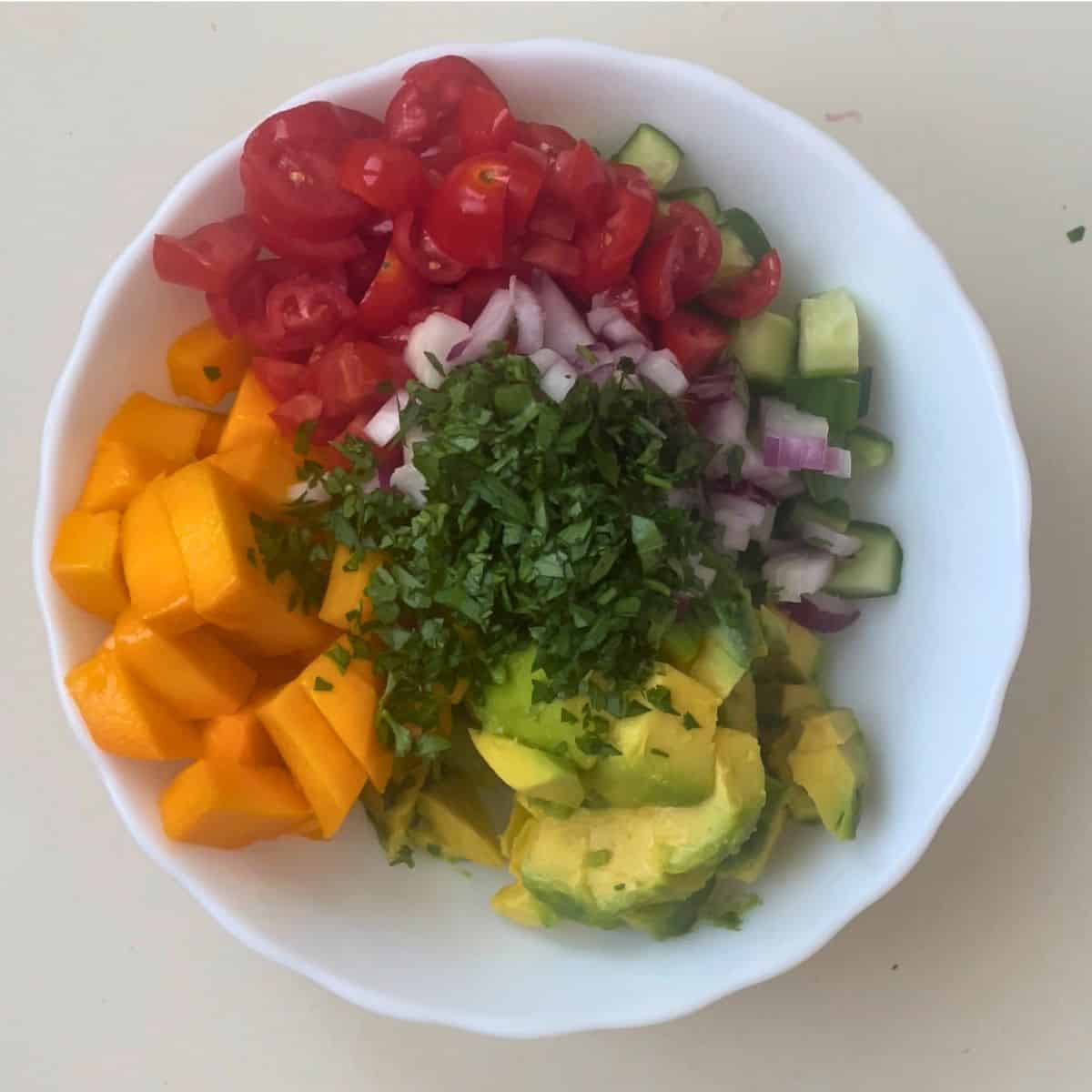A white bowl with mango salad ingredients.