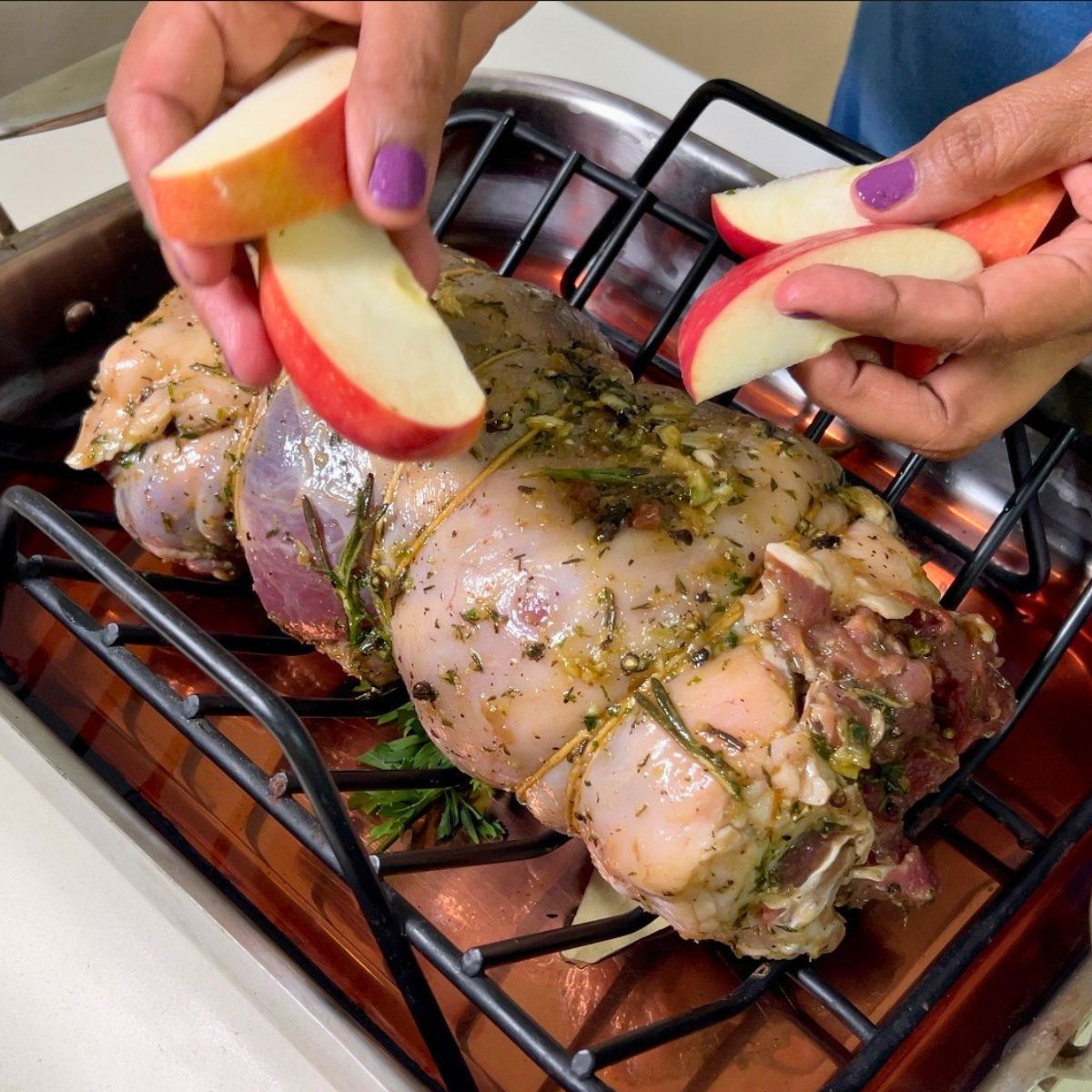Adding apple slices to the roasting lamb.