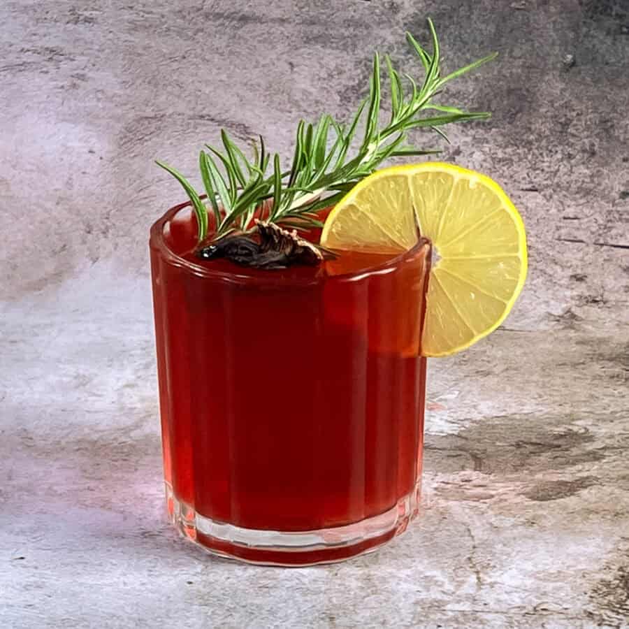 A glass with deep red cocktail made with hibiscus.