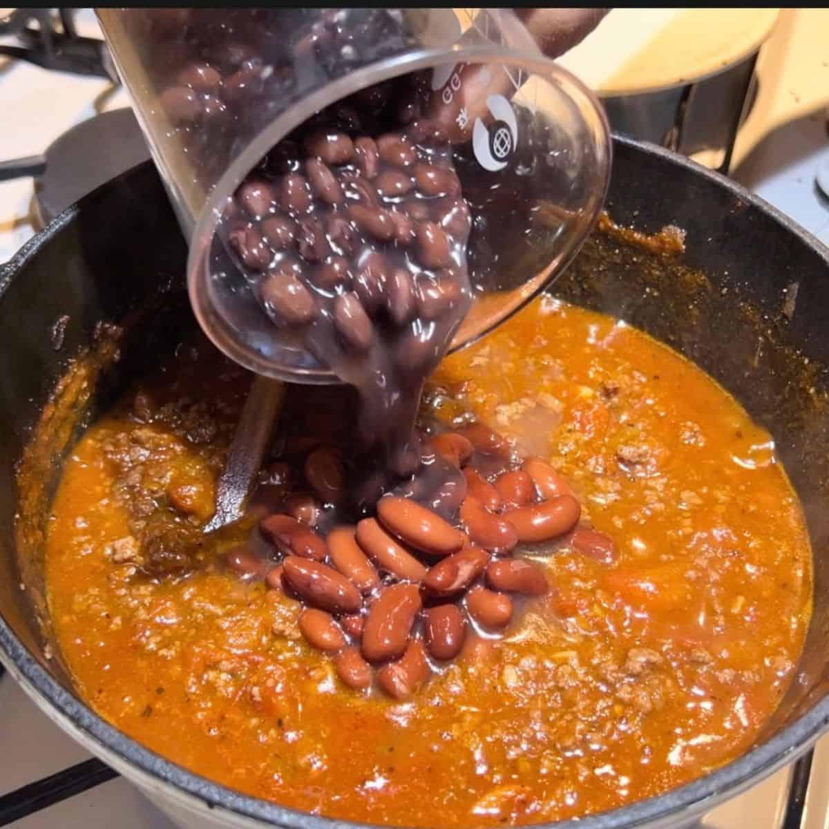 Adding beans to the ground beef chli.