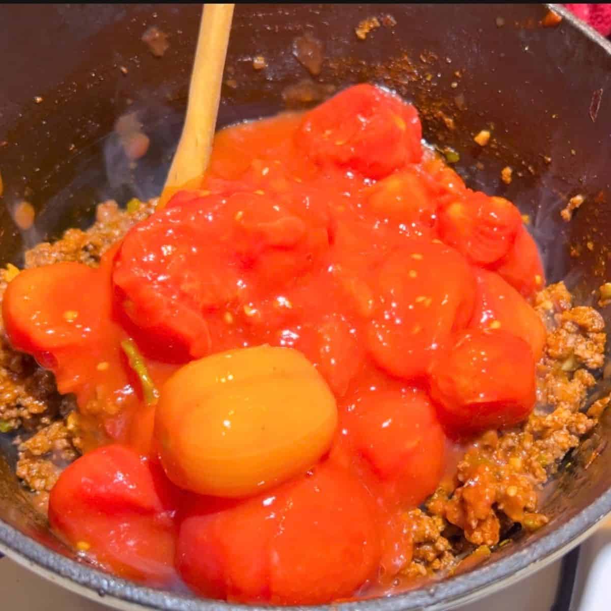 Adding tomatoes and tomato paste to the cast iron skillet.