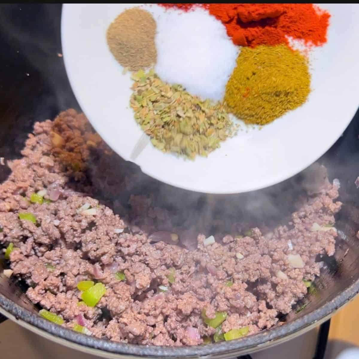 Adding spices to the cast iron skillet with chili.